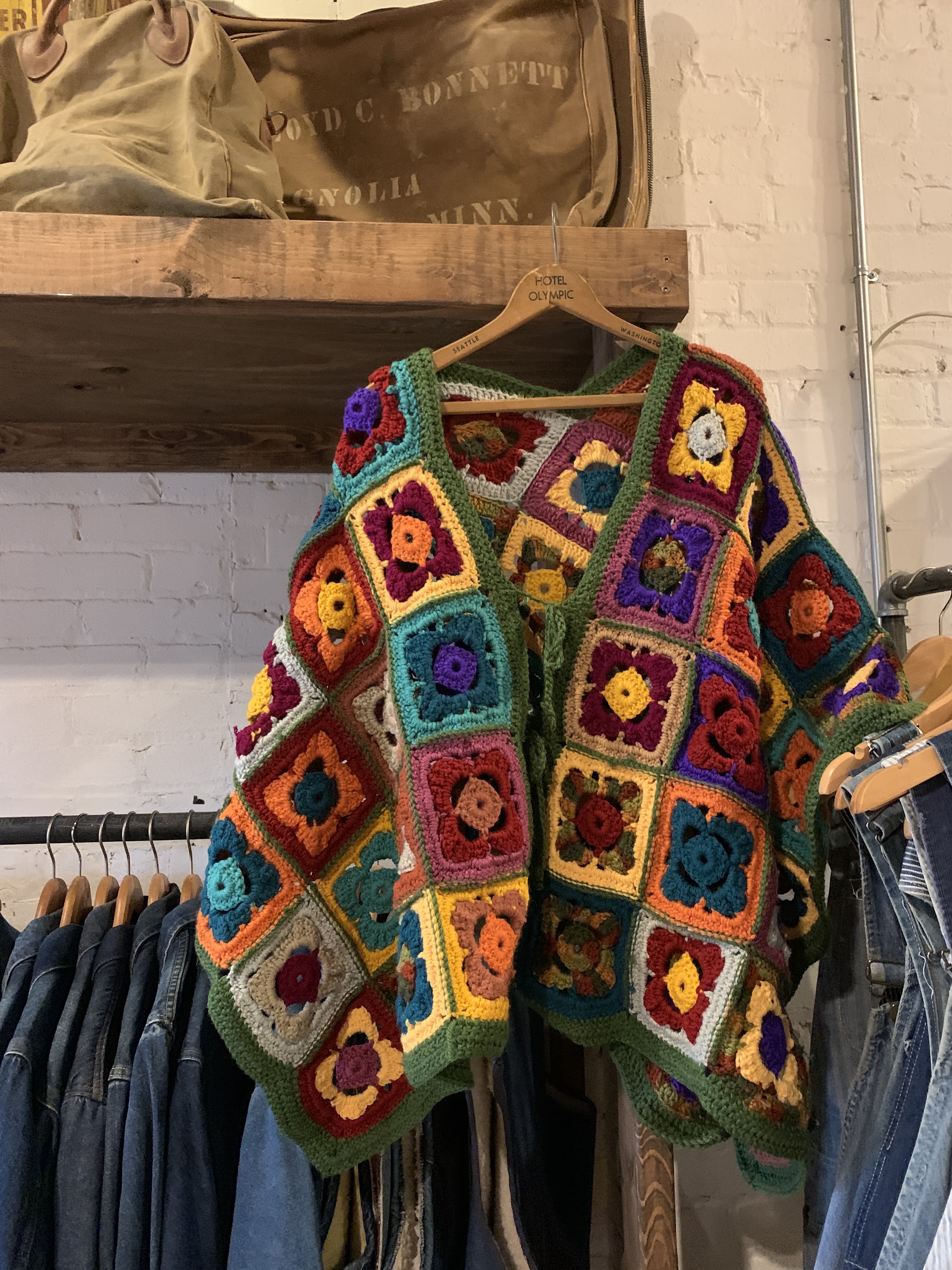 Colourful granny-square crochet cardigan hanging above a row of denim