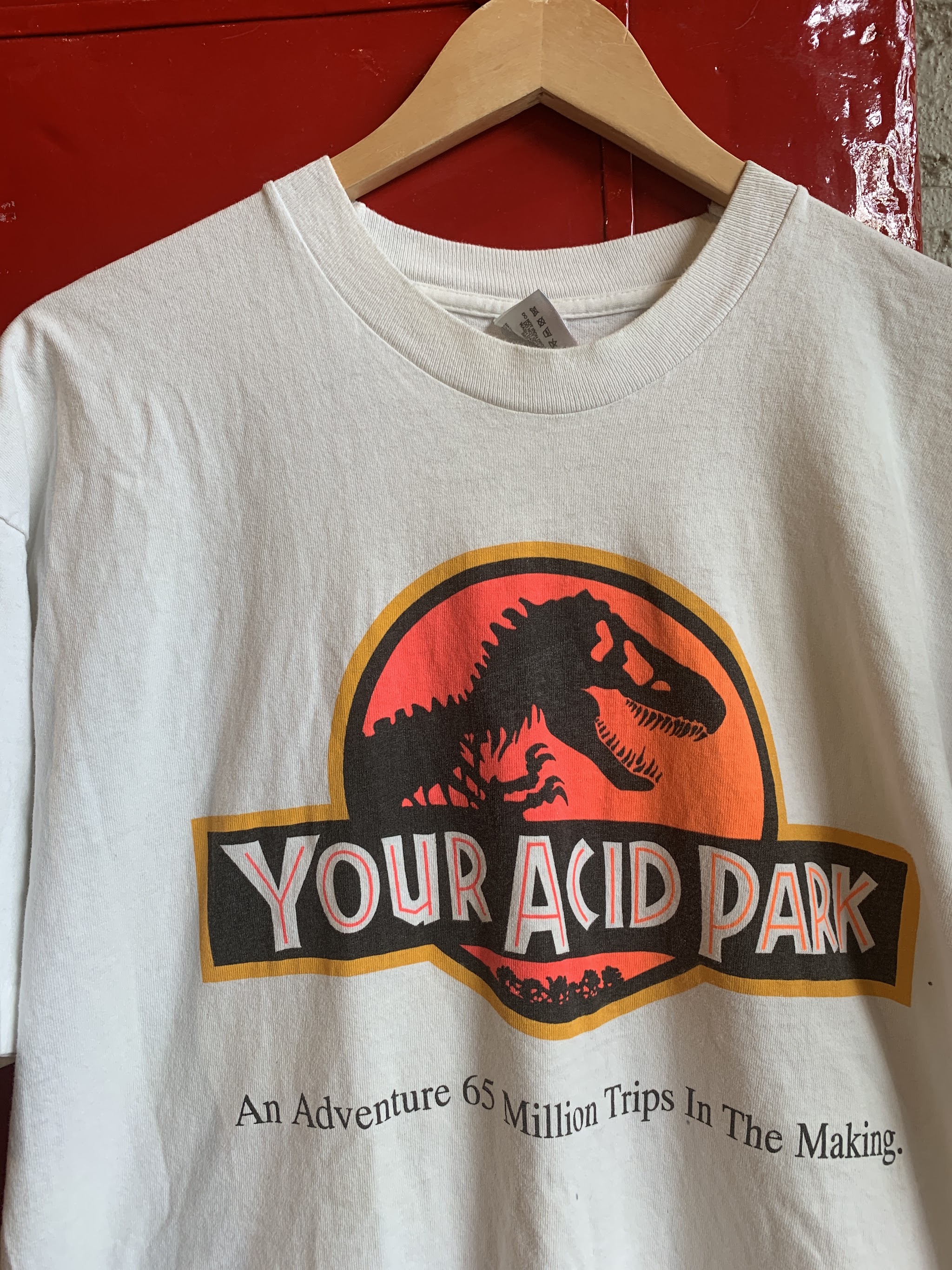 Your Acid Park graphic t-shirt on a hanger against a red wall