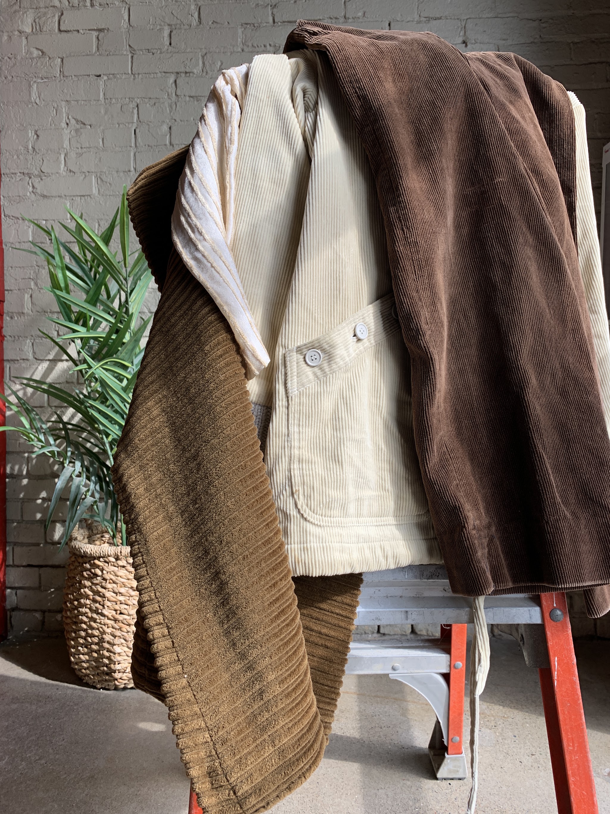 Cream chore jacket and brown corduroy jacket draped over a red step ladder