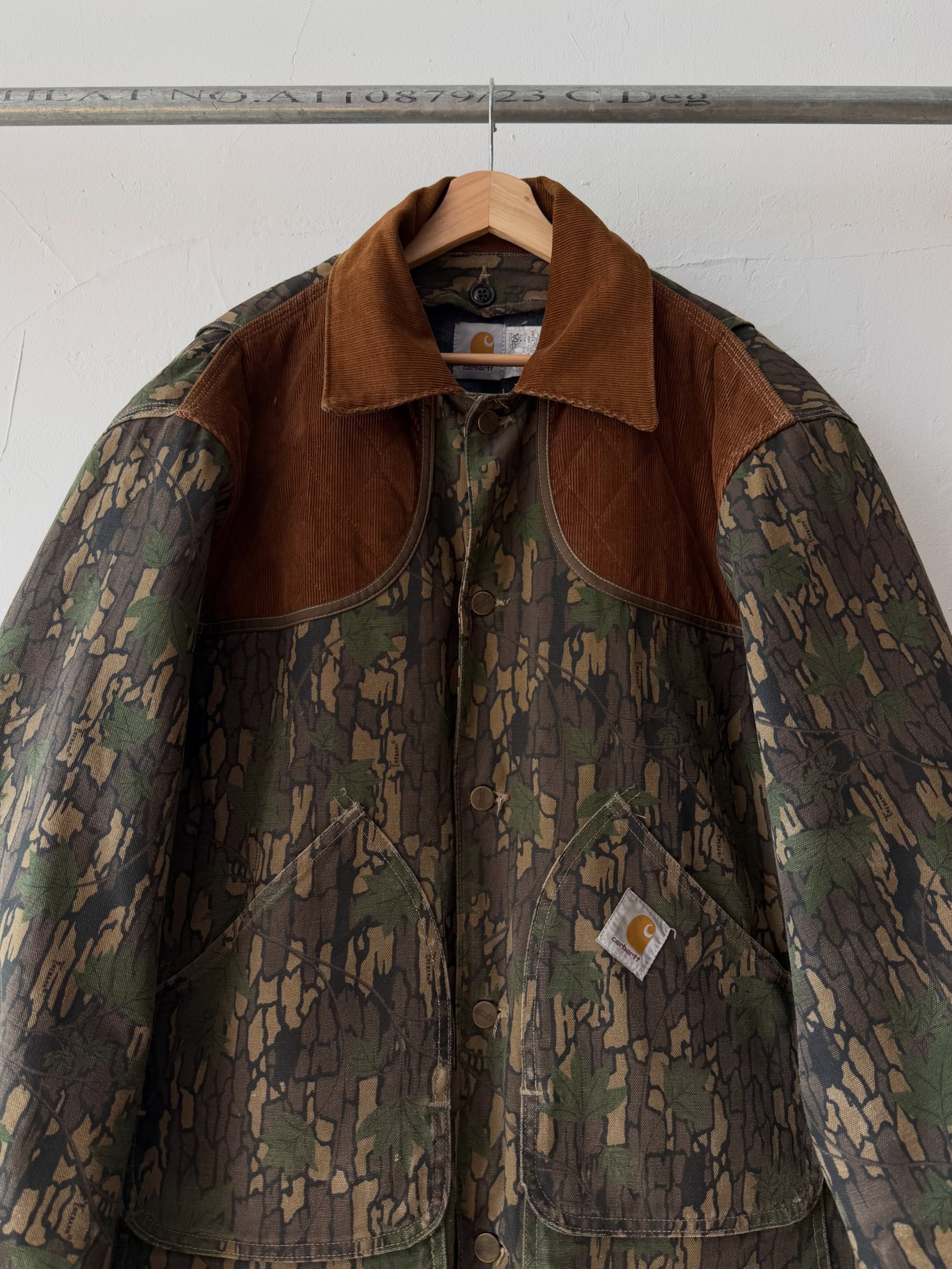 Camouflage 1990s Carhartt hunting jacket with brown corduroy collar on a hanger