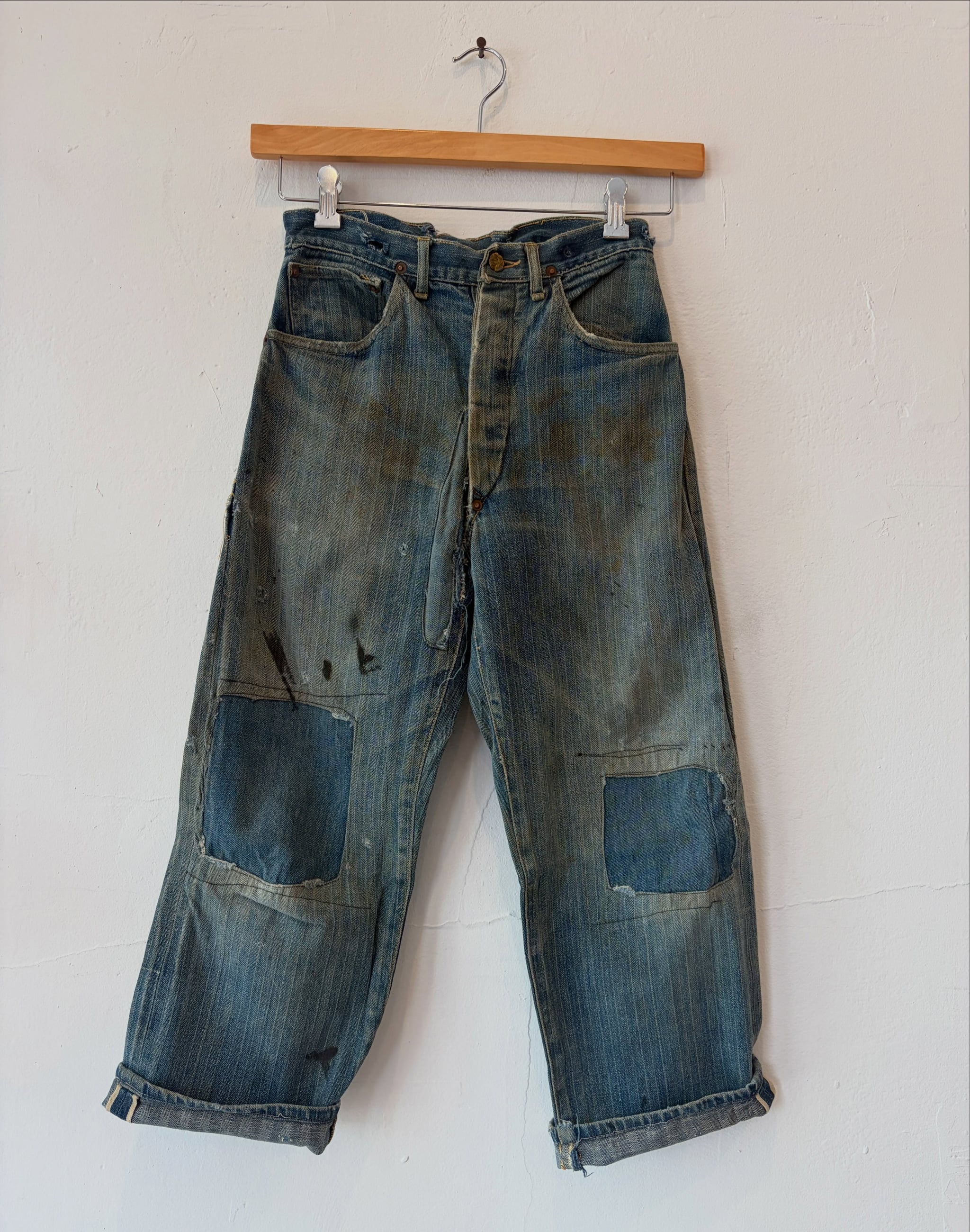 Small pair of patched 1920s OshKosh denim work pants on a wooden hanger