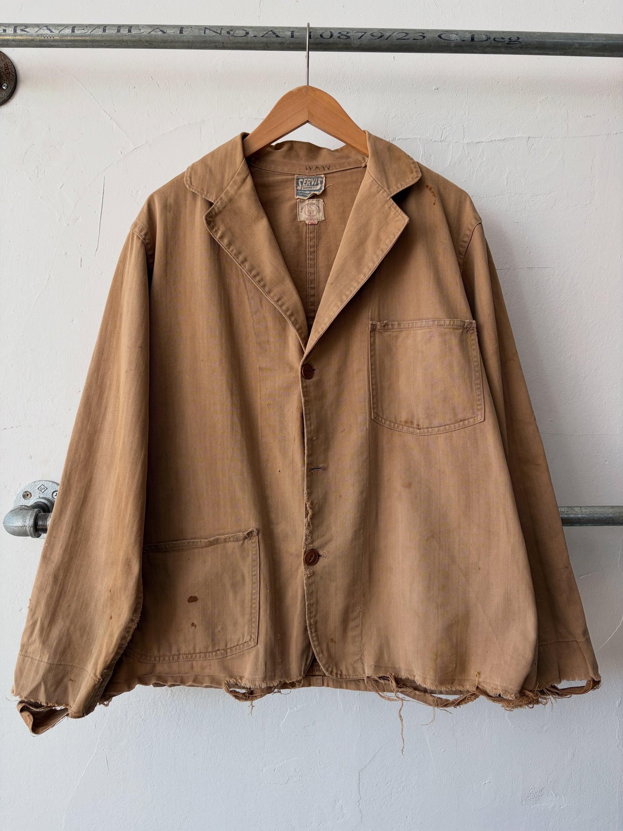 Tan 1930s twill shop jacket with two patch pockets on a hanger